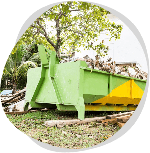 A green dumpster with yellow handles in the grass.